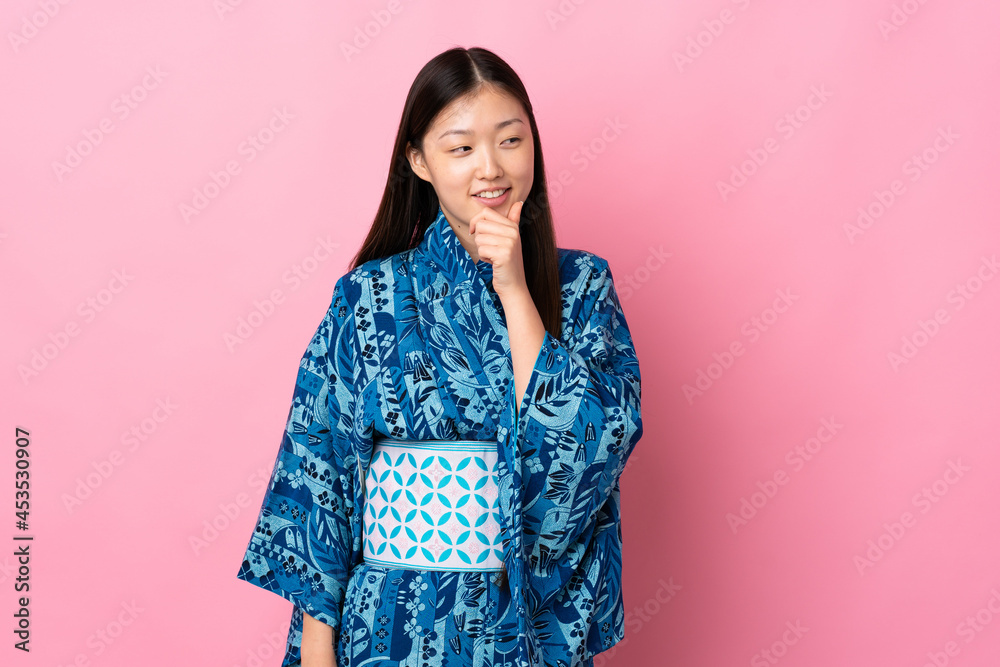 Young Chinese girl wearing kimono over isolated background looking to the side and smiling Young Chinese girl wearing kimono over isolated background looking to the side and smiling
