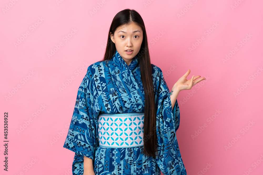 Young Chinese girl wearing kimono over isolated background making doubts gesture Young Chinese girl wearing kimono over isolated background making doubts gesture