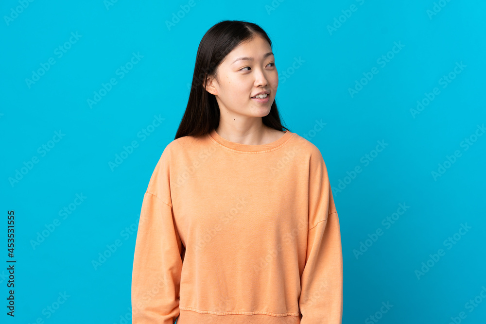 Young Chinese girl over isolated blue background looking to the side and smiling Young Chinese girl over isolated blue background looking to the side and smiling
