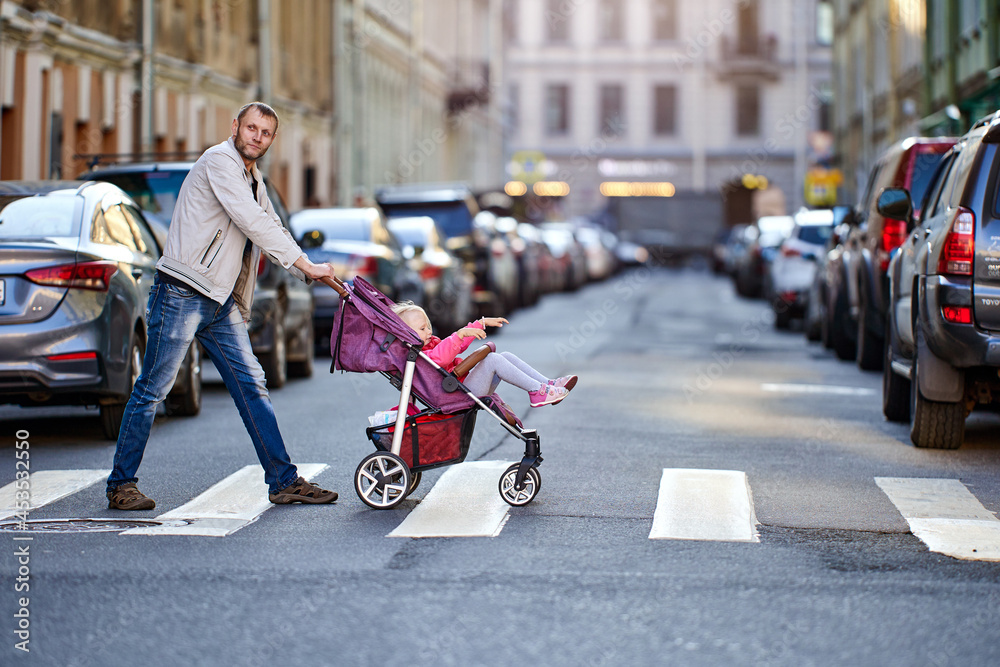 Obraz premium Girl 3 years old in baby carriage and father on crosswalk near traffic.