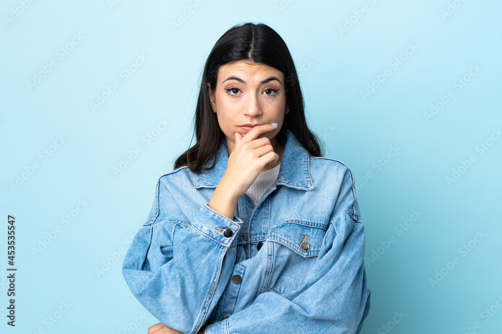 Young brunette girl over isolated blue background surprised and shocked while looking right