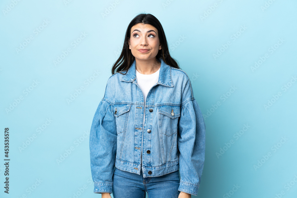 Young brunette girl over isolated blue background having doubts while looking up Young brunette girl over isolated blue background having doubts while looking up