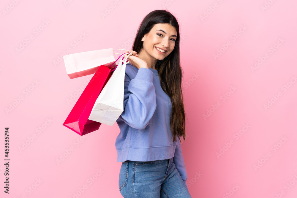 Young brunette girl over isolated pink background holding shopping bags and smiling