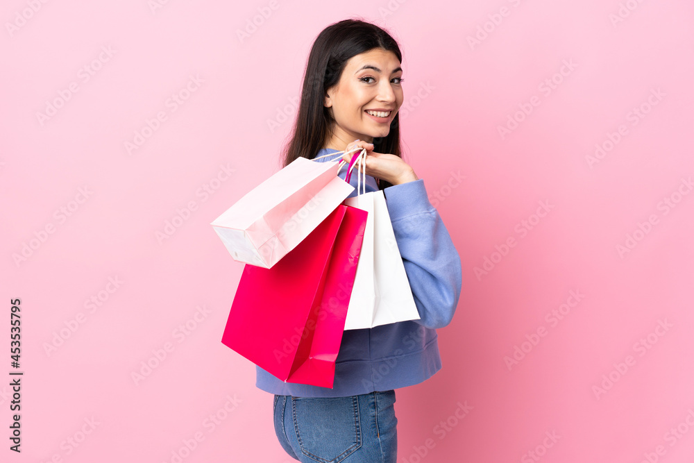 Young brunette girl over isolated pink background holding shopping bags and smiling Young brunette girl over isolated pink background holding shopping bags and smiling