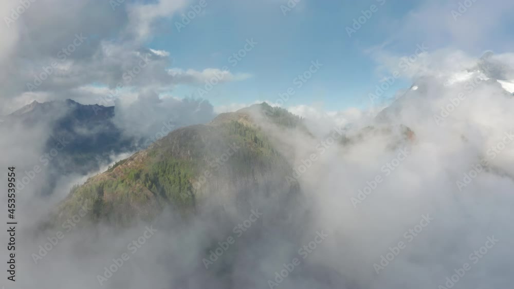 Aerial view of a drone flying over green forest on massive steep mountain covered by thick fog clouds at sunrise or sunset. Travel USA and Canada boarder nature park. Bird eye view through cloudscape Aerial view of a drone flying over green forest on massive steep mountain covered by thick fog clouds at sunrise or sunset. Travel USA and Canada boarder nature park. Bird eye view through cloudscape