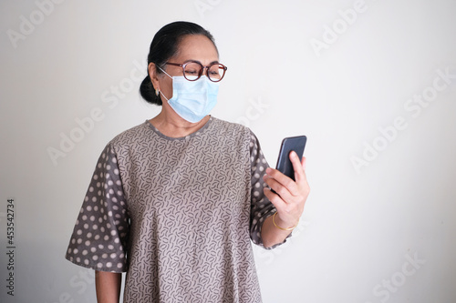 Elderly Asian woman wearing protective medical mask while looking to her mobile phone photo