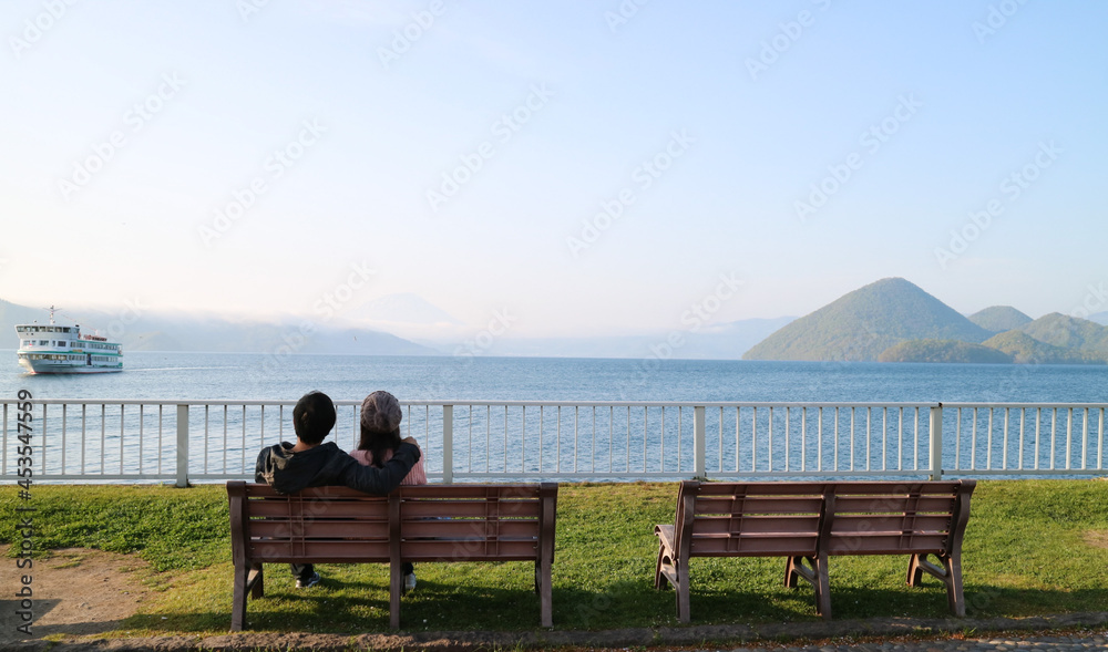 The morning scenery of the sea, sky, mountains, trees, boats and a young couple at Lake Toya in Hokkaido, Japan gives a feeling of freshness and relaxation.