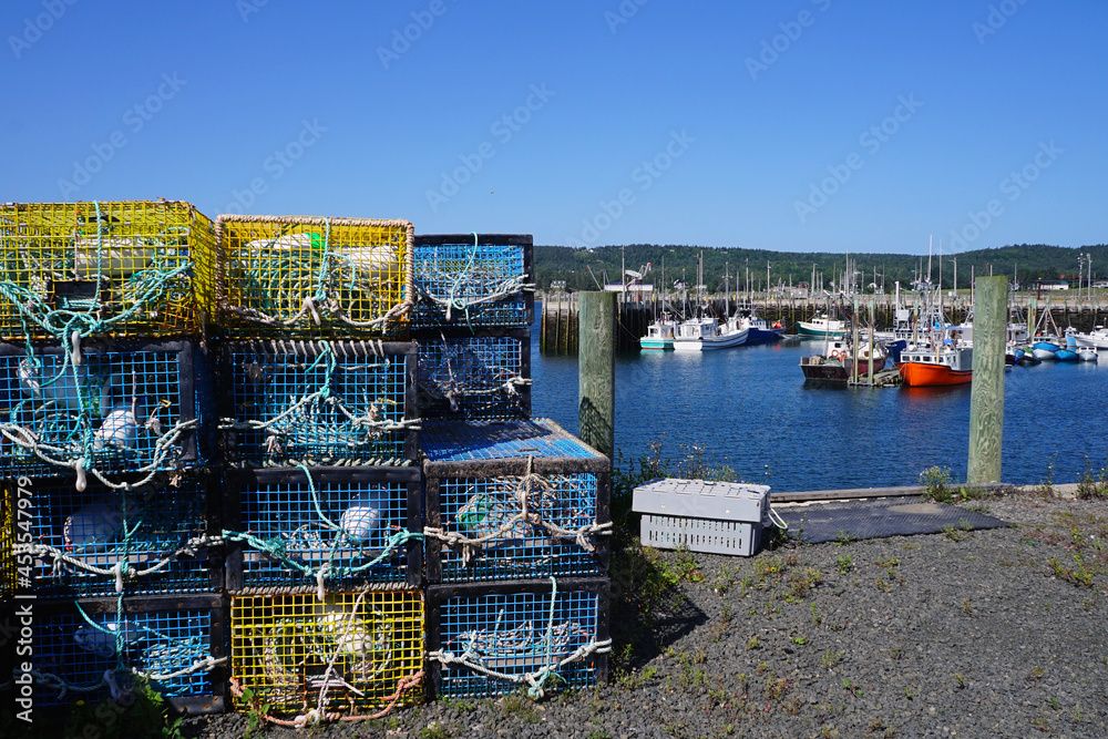 Stacked lobster traps on the pier with fishing boats moored in the background at North Head on Grand Manan Island, New Brunswick Stacked lobster traps on the pier with fishing boats moored in the background at North Head on Grand Manan Island, New Brunswick
