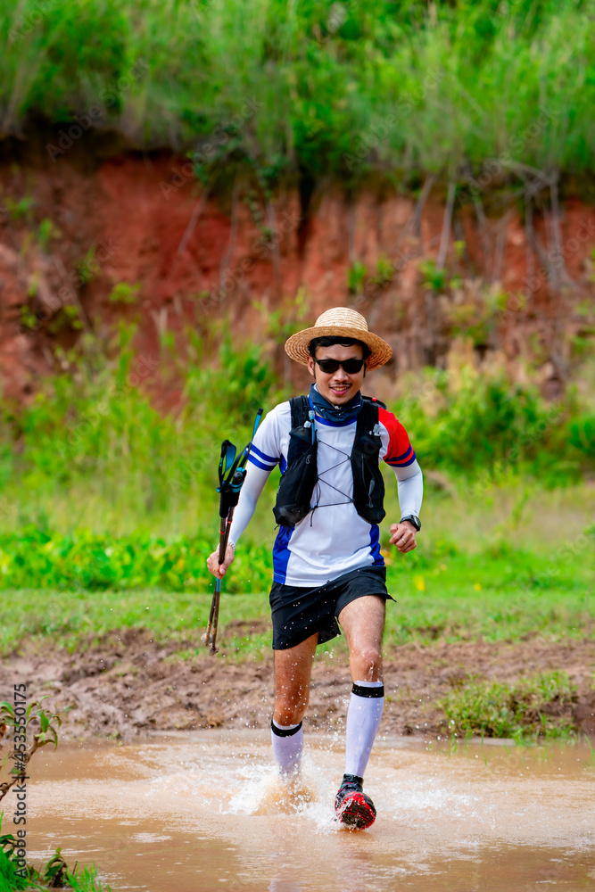 Asian men's trail runners wearing sportswear and equipment. Practicing running and wading through water, running on a dirt path On a day when the sky is clear