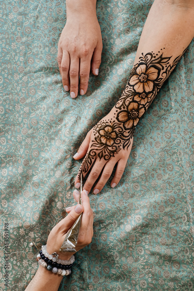 Foto Stock Artist applying henna tattoo on women hands. Mehndi is  traditional Indian decorative art, Hand with floral mehendi. Beauty drawing  for weddings and festivals using paste from powdered dry plant