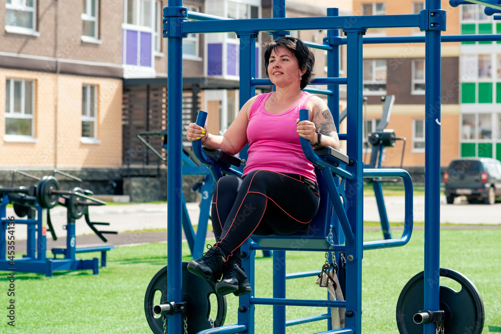 young woman performs exercises outdoors using street fitness combo machine young woman performs exercises outdoors using street fitness combo machine