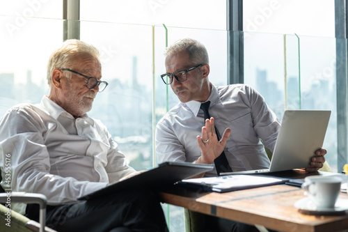 Picture of young business man taking to his older business partner. They are in white shirt and black tie. They are in a hotel lobby. 