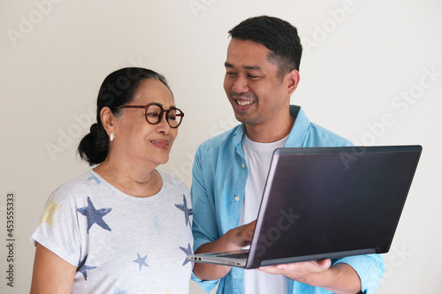 Young Asian man showing something using his laptop to elderly woman photo