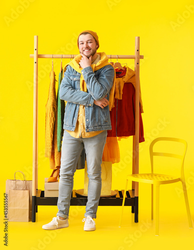Male stylist near rack with clothes on color background