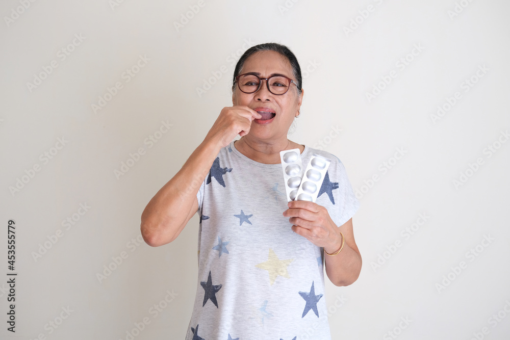Elderly Asian woman holding multi vitamin tablet and consume it to keep her body healthy Elderly Asian woman holding multi vitamin tablet and consume it to keep her body healthy