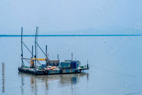 Small barge with yellow crane moored in harbor with hazy sky in background.