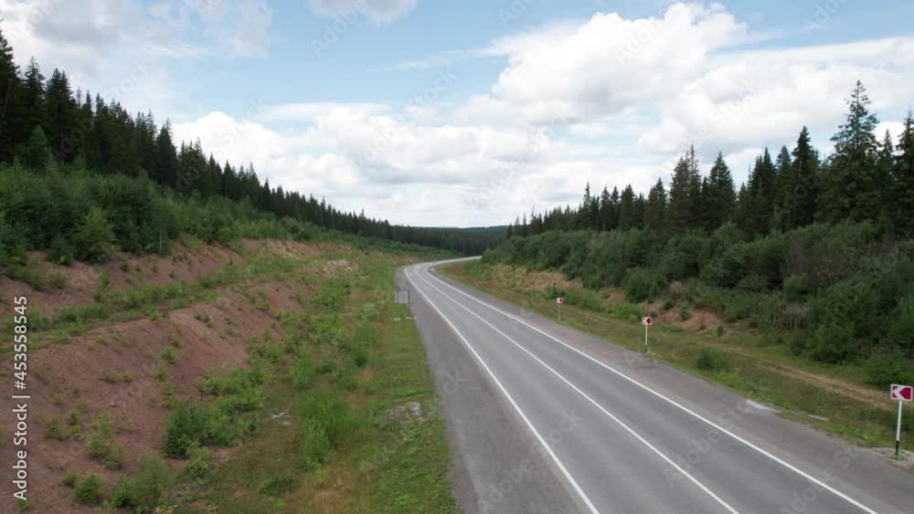 Aerial view of scenic road between green trees with pines on a sunny summer morning. Nature landscape in Siberia, Russia. A road passing through a coniferous forest, aerial shot from a drone. Aerial view of scenic road between green trees with pines on a sunny summer morning. Nature landscape in Siberia, Russia. A road passing through a coniferous forest, aerial shot from a drone.