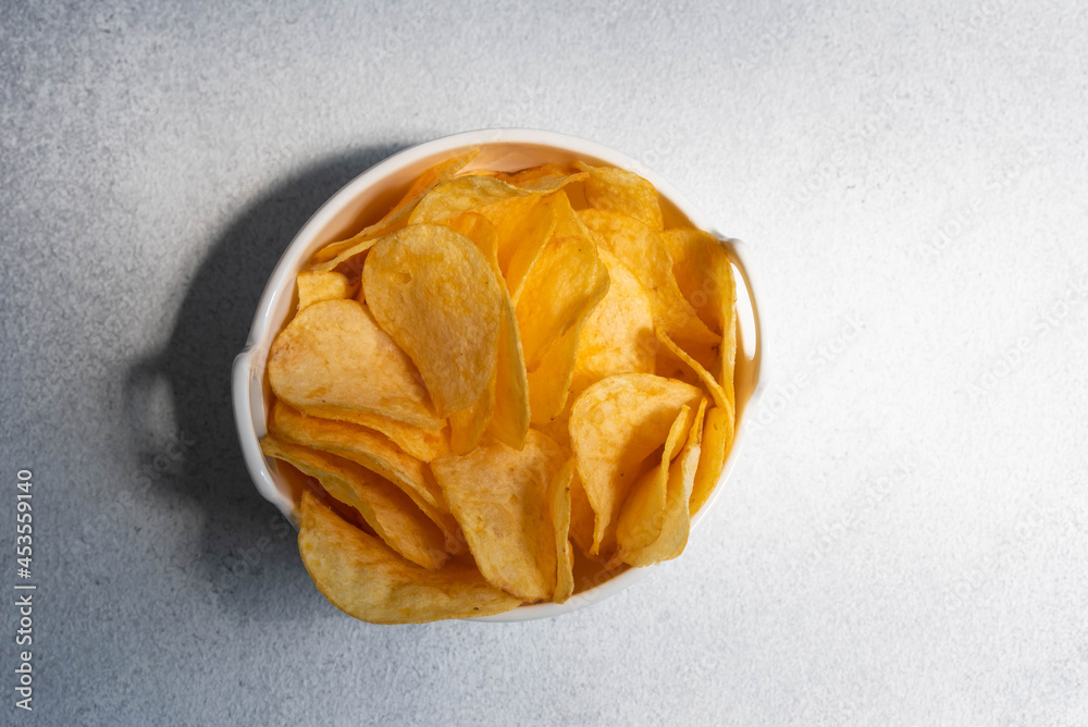 Crispy salty potato chips or crisps in bowl on white background. Unhealthy food concept. Crispy salty potato chips or crisps in bowl on white background. Unhealthy food concept.