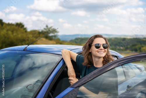 Young happy female driver resting near her car enjoying view of summer nature. Travel destinations