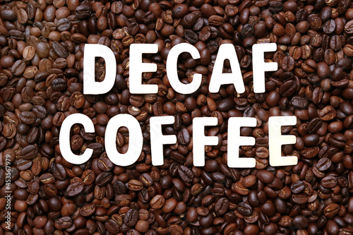 Decaf coffee word on roasted coffee beans background. Concept of decaffeinated coffee or low caffeine coffee.