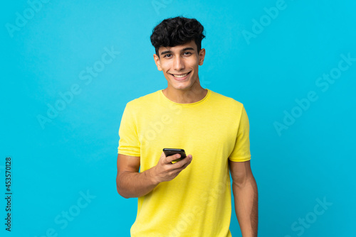 Young Argentinian man isolated on background sending a message with the mobile