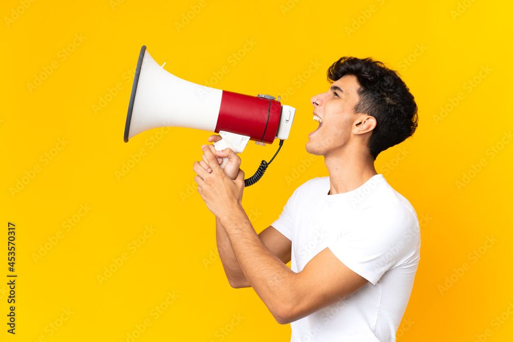 Young Argentinian man isolated on yellow background shouting through a megaphone to announce something in lateral position Young Argentinian man isolated on yellow background shouting through a megaphone to announce something in lateral position