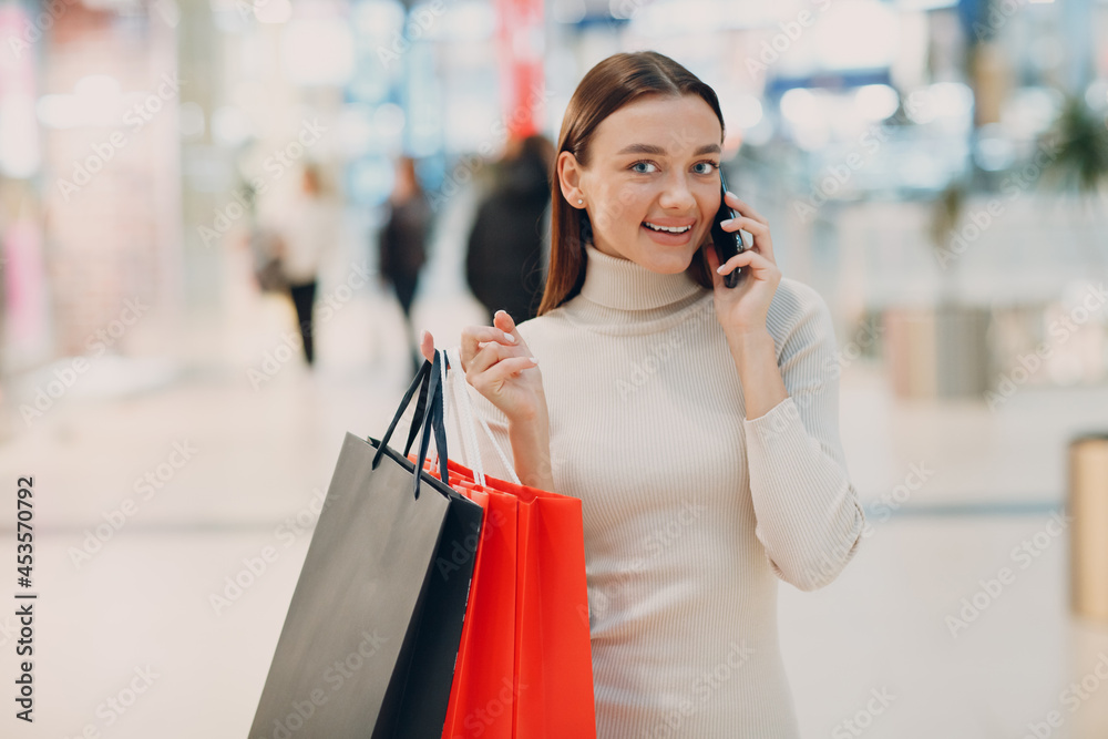 Positive young adult woman carrying paper shopping bags and mobile phone Positive young adult woman carrying paper shopping bags and mobile phone