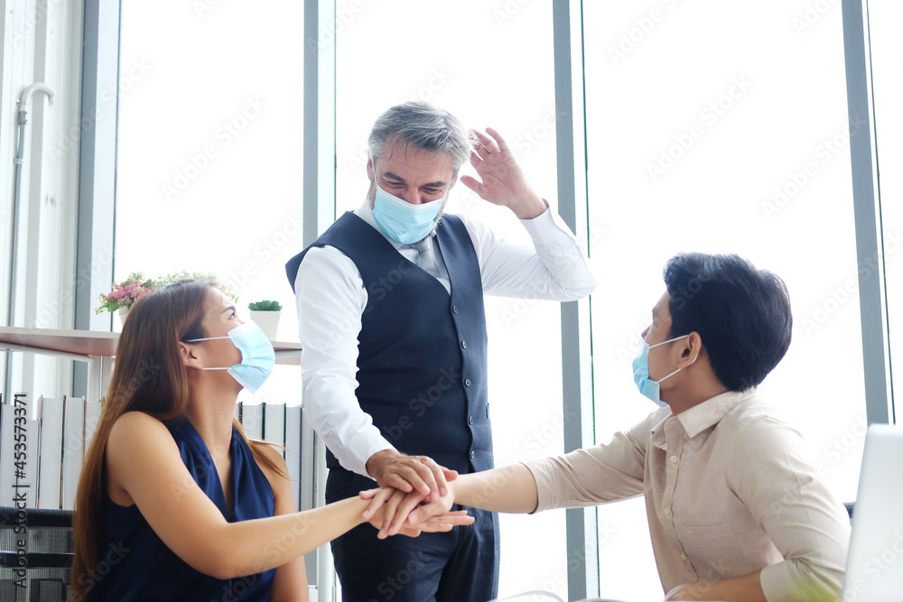 Obraz premium Asian and Caucasian businesspeople teamwork wearing mask preventing for covid 19 virus and joining hands together for successful in jobs and business after meeting and branistom with partner.