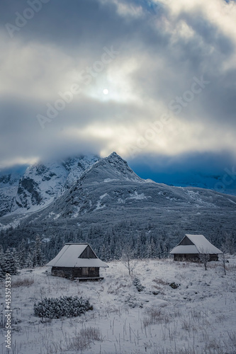 Majestic Hala Gąsienicowa Valley in winter, Tatra Mountains, Poland. Small wooden buildings covered with fresh winter snow. Selective focus on the peak in the distance, blurred background.