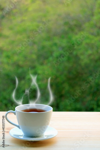 Cup of Hot Tea with Rising Steam on Blurry Green Foliage in Background