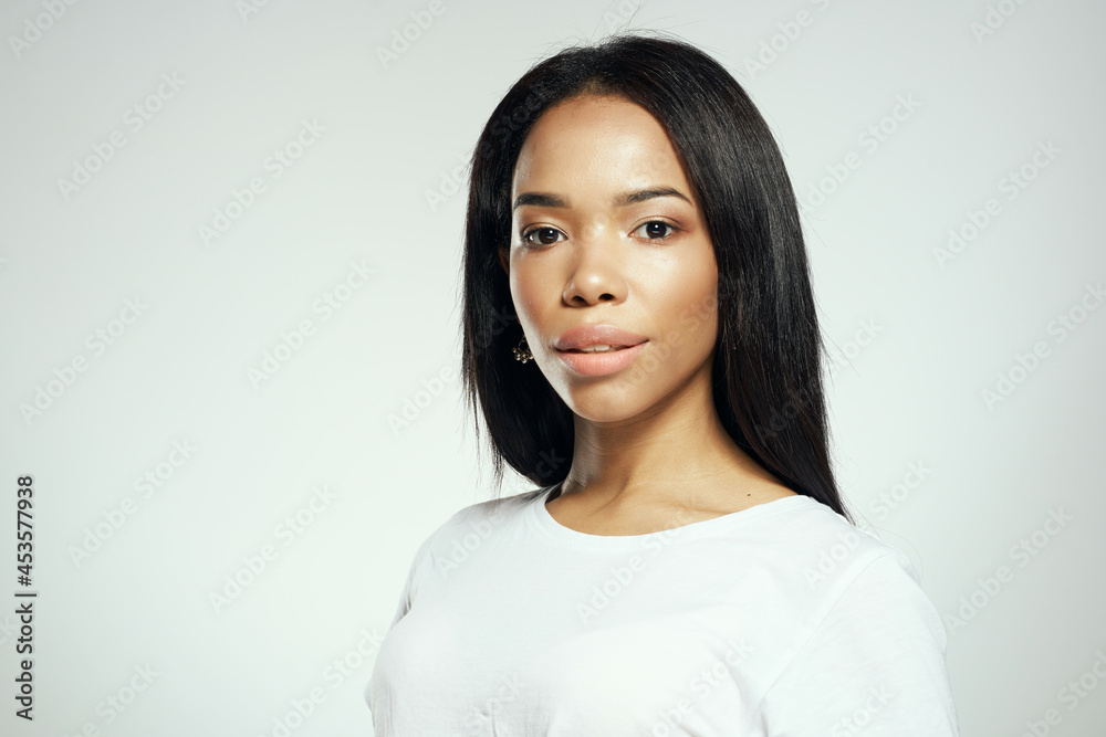 woman in white t-shirt black long hair earrings jewelry light background