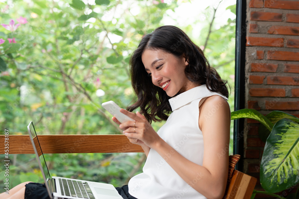 Naklejka premium Young smiling female reading text message on mobile phone while resting in coffee shop interior