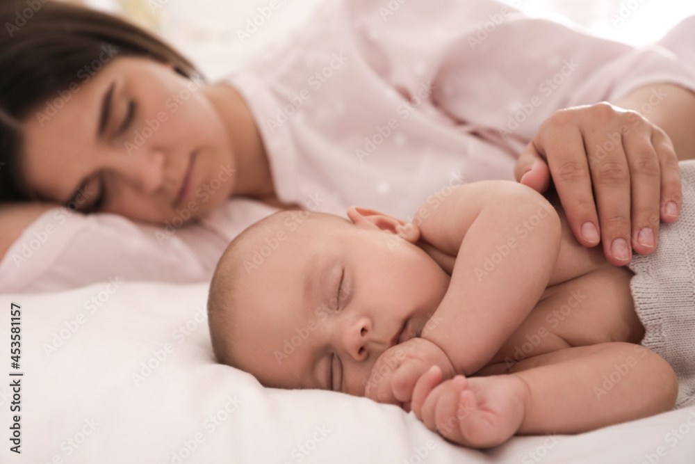 Young mother resting near her sleeping baby on bed at home Young mother resting near her sleeping baby on bed at home
