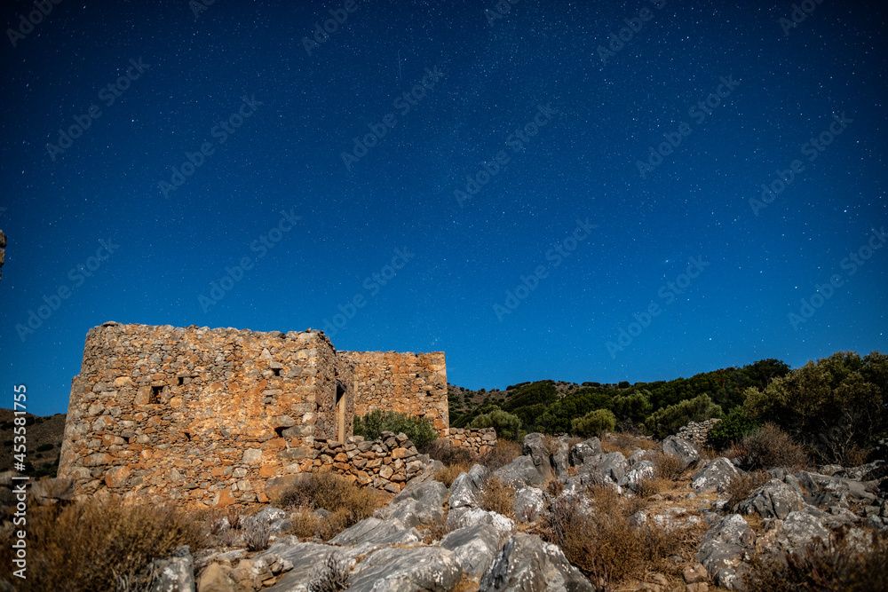 ancient stone mills and their ruins on the slopes of the mountains on the island of Crete against the background of the starry sky