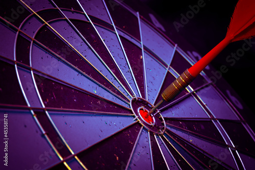 Close up shot of the dart arrow hit on bulleyes of dartboard to represent that the business reached the target of company with dark tone picture style. Target and goal as concept.	
