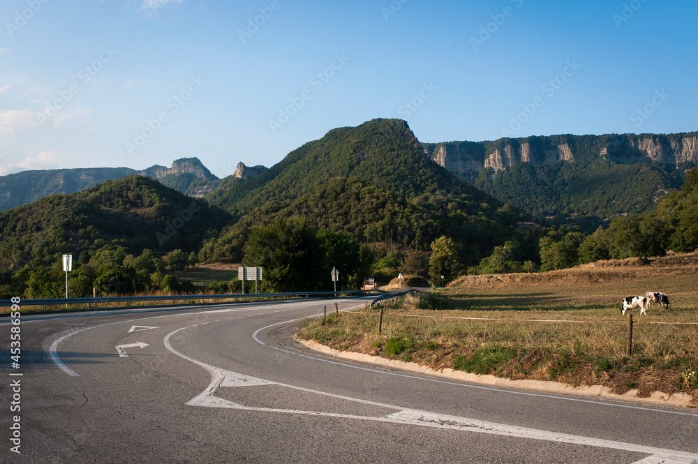 Una carretera pasa por un terreno montañoso con un prado con vacas pastando Una carretera pasa por un terreno montañoso con un prado con vacas pastando