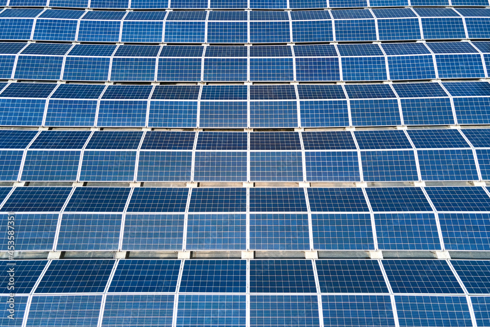 Aerial view of solar power plant with blue photovoltaic panels mounted on industrial building roof for producing green ecological electricity. Production of sustainable energy concept. Aerial view of solar power plant with blue photovoltaic panels mounted on industrial building roof for producing green ecological electricity. Production of sustainable energy concept.