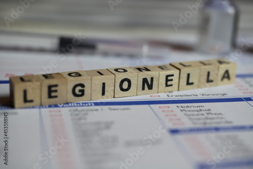 Viersen, Germany - June 1. 2021: Closeup of word legionella on laboratory requisition slip with syringe and vial (selective focus on upper right part of text block with letter O)