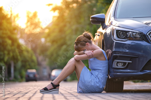 Young tired woman sitting beside car waiting for someone. Travelling and vacations concept.