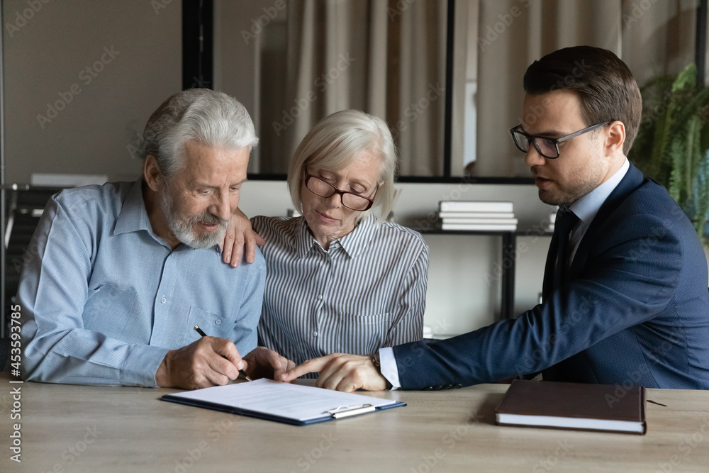 Fototapeta premium Mature couple signing contract, making insurance investment deal with manager broker or realtor in office, businessman in glasses consulting senior family, pointing finger at document agreement