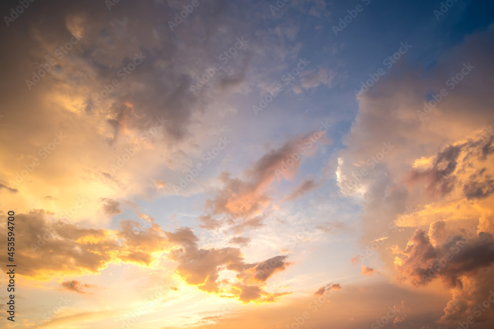 Dramatic cloudy sunset landscape with puffy clouds lit by orange setting sun and blue sky.