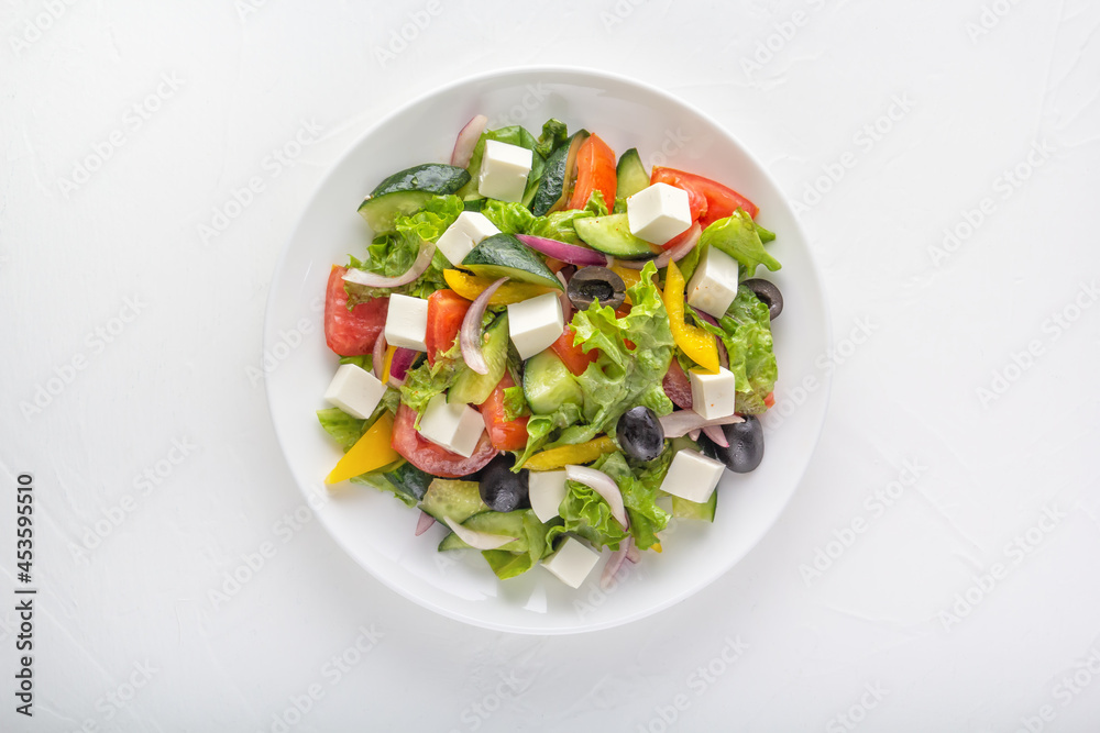 Greek salad of fresh cucumber, tomatoes, bell peppers, lettuce, red onions, feta cheese and olives with olive oil in a white plate on a light background. Healthy eating. Top view