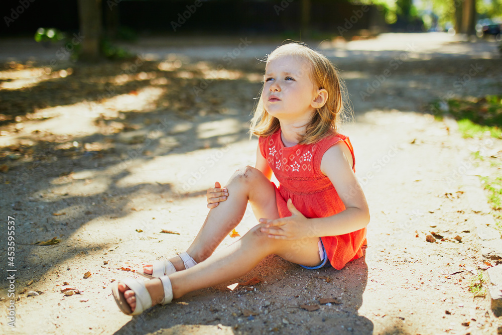 Cute little girl sitting on the ground after falling down Stock Photo