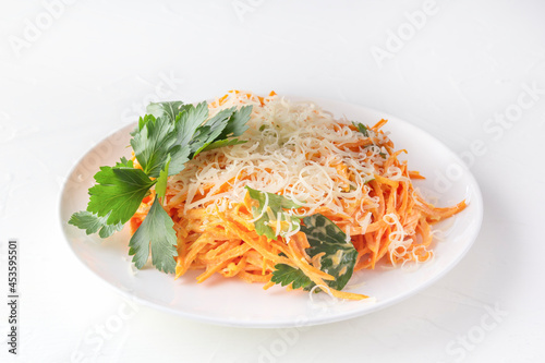 Fresh carrot salad with cheese and herbs in a white plate on a white plate. Close up