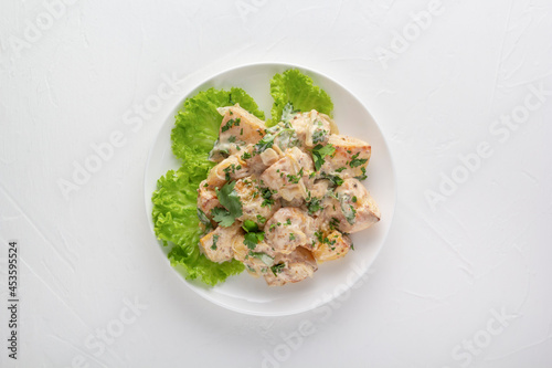 Baked potatoes in sour cream sauce with herbs are placed in a white plate on lettuce leaves. View from above