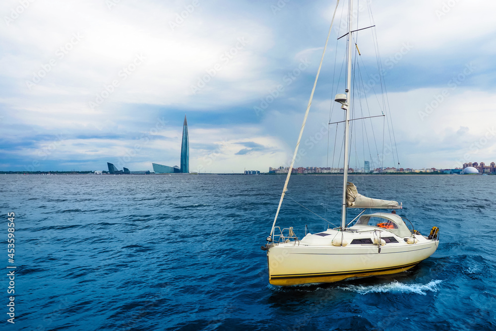 Sailboat in the Gulf of Finland, Baltic Sea. Dramatic clouds and sky, storm clouds over sea. Residential areas and Lakhta in St. Petersburg in the background