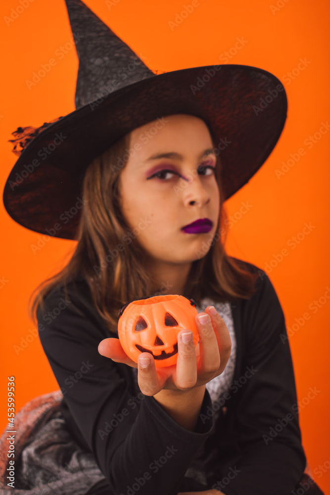 Studio portrait of a little witch with a little pumpkin in her hand on Halloween Studio portrait of a little witch with a little pumpkin in her hand on Halloween