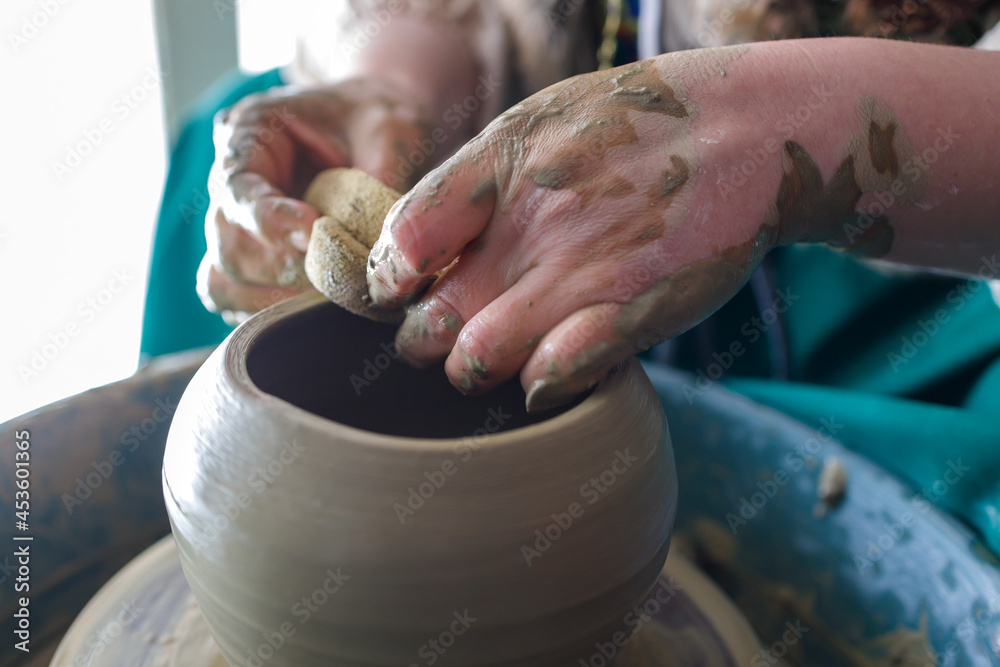 close-up of a potter's hands while working on a potter's wheel. dirty hands of the master. active rest in the pottery workshop