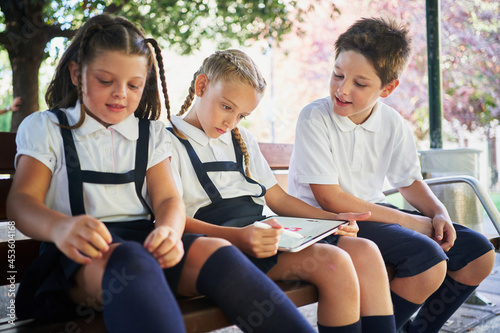 Three school children sitting in bank drawing on tablet