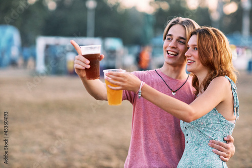 A young couple in love is hugging and holding a beer. They are pointing at something interesting.